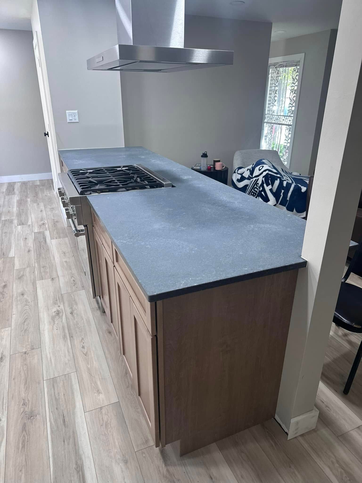 Modern kitchen with gray island, wood cabinets, stovetop, and stainless range hood