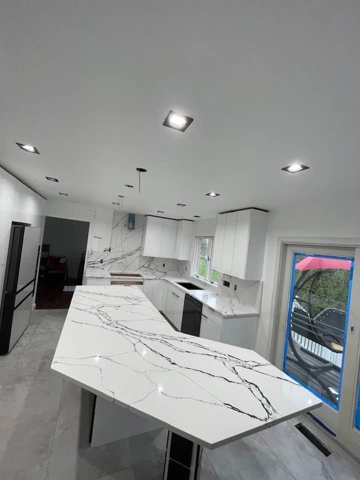 Modern white kitchen with marble countertops, island, black appliances, and recessed ceiling lights