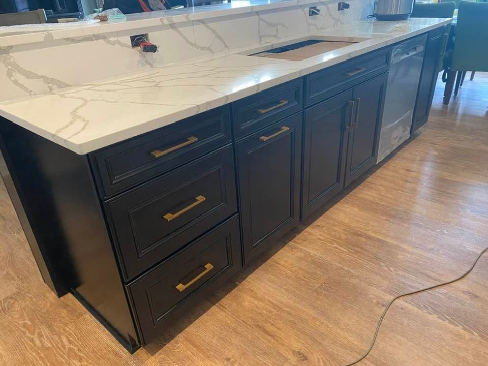 Black kitchen island with white marble-look countertop and brass handles on a wood floor.
