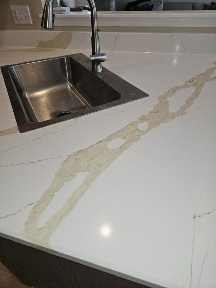 White kitchen countertop with a stainless steel sink and a long beige stain or spill.