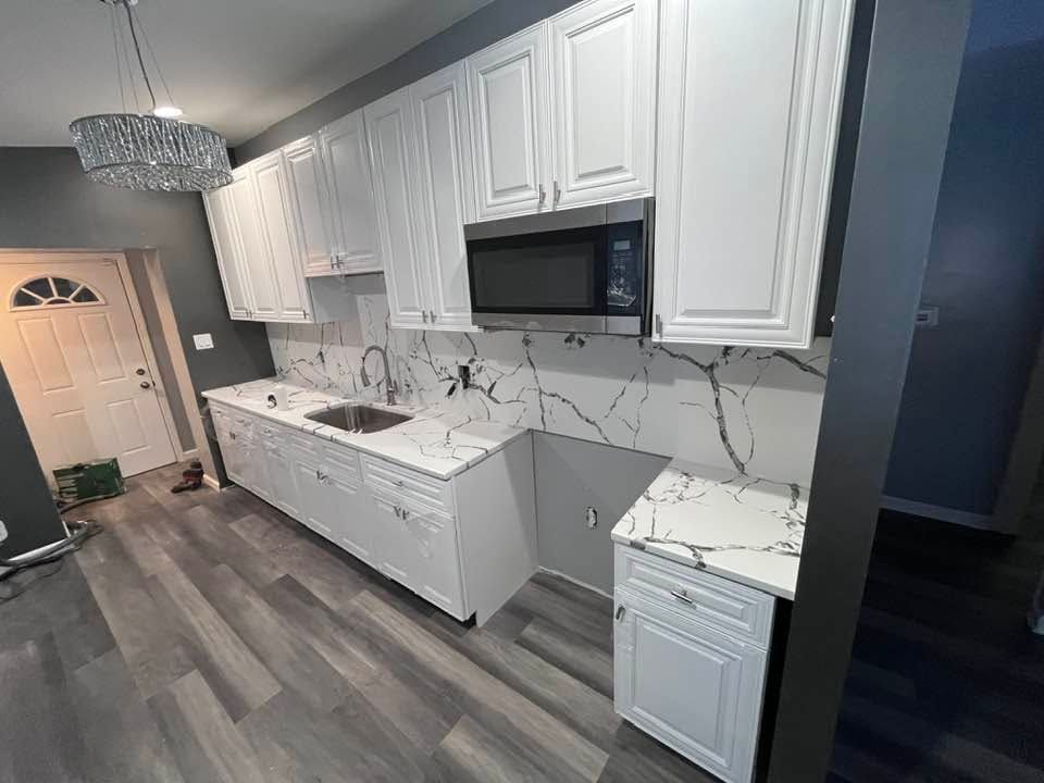 Modern white kitchen with marble countertops, white cabinets, gray flooring, and stainless microwave