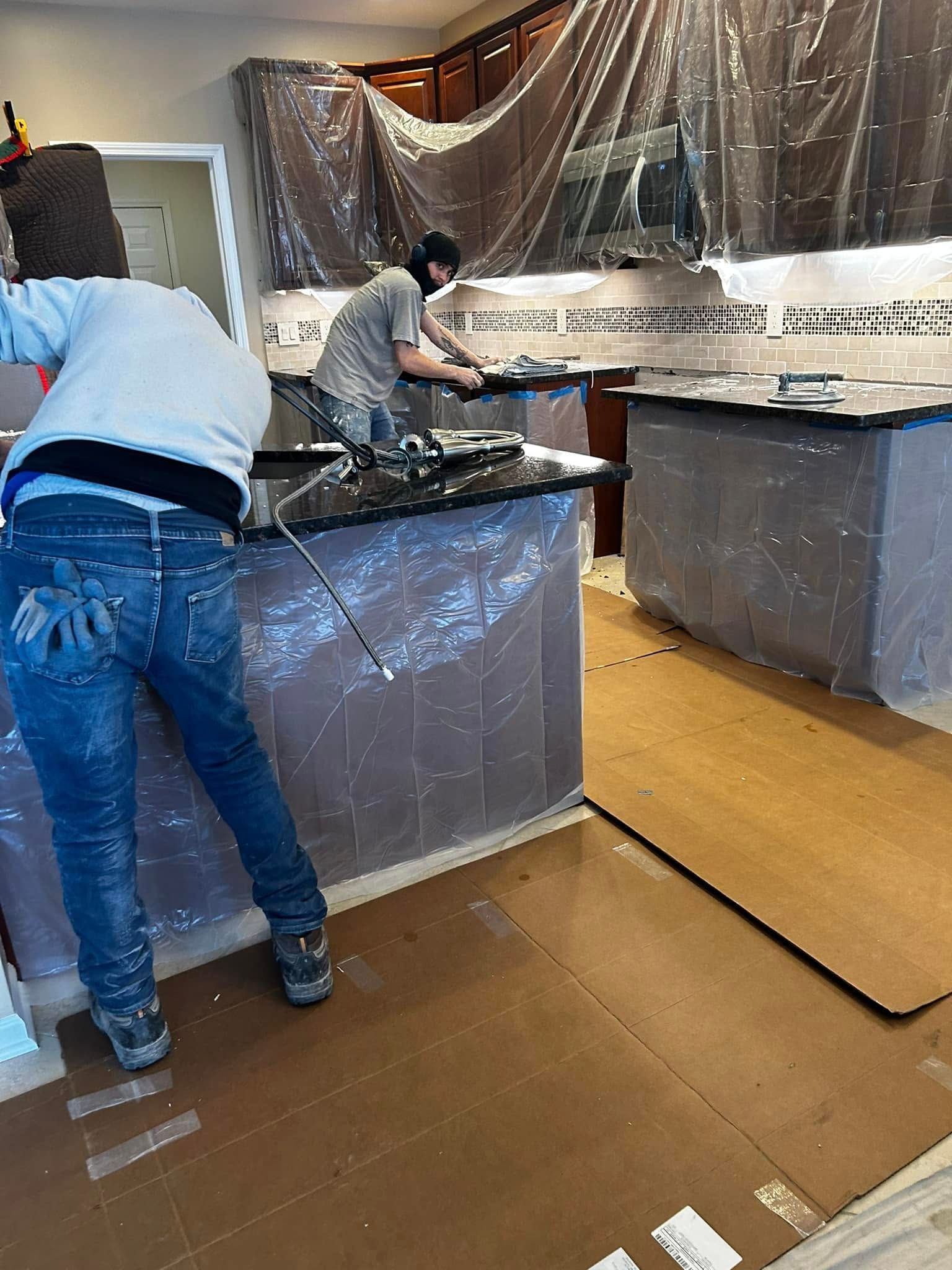 Workers covering kitchen counters and appliances with plastic sheeting during renovation