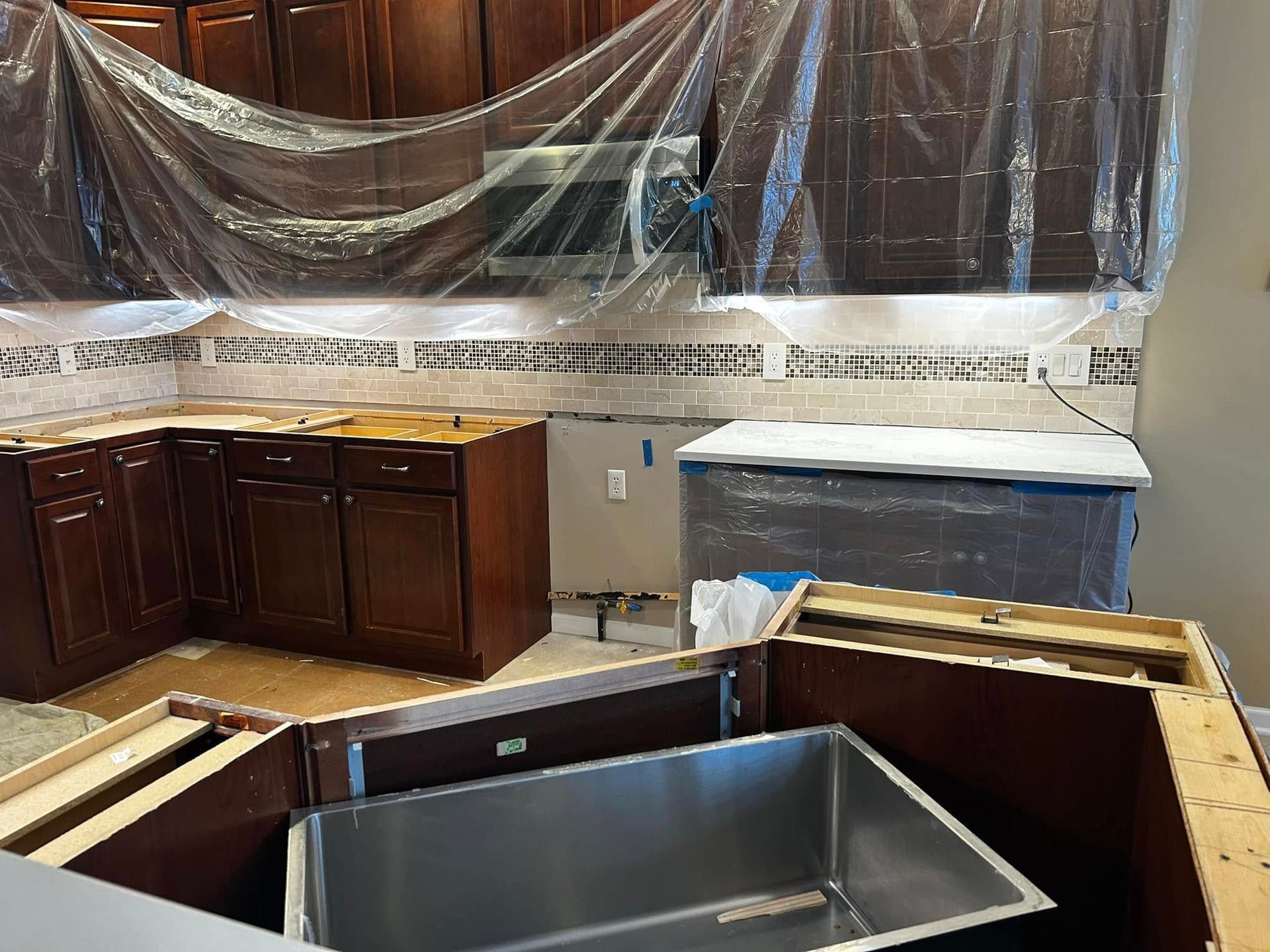 Kitchen under renovation with cabinets, plastic-covered counters, and a stainless steel sink installed in an island.