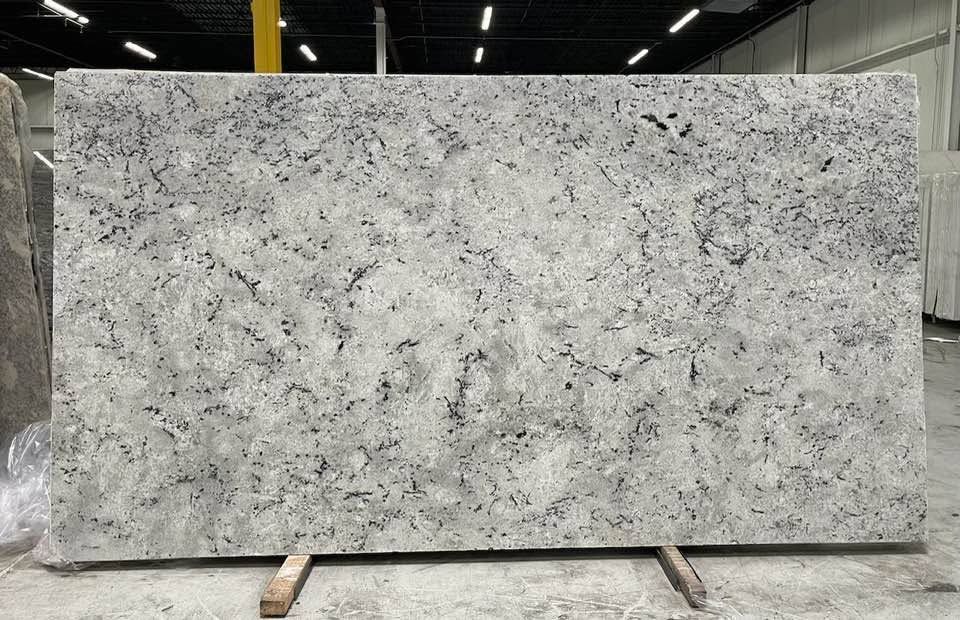 Large light-gray speckled granite slab standing upright in a warehouse or stone yard