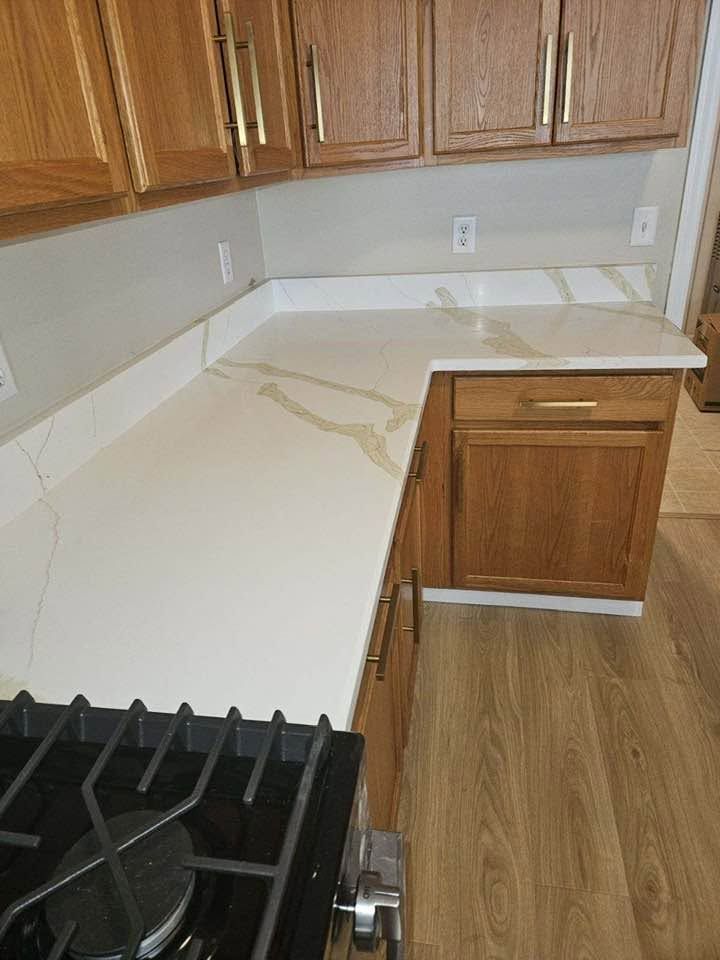 Kitchen countertop with white surface, wood cabinets, and black gas stove in the foreground.