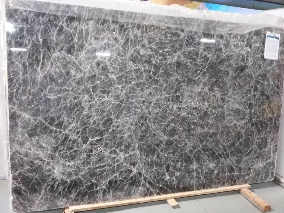 Large gray marble slab with white veining leaning on wooden supports in a warehouse or showroom.