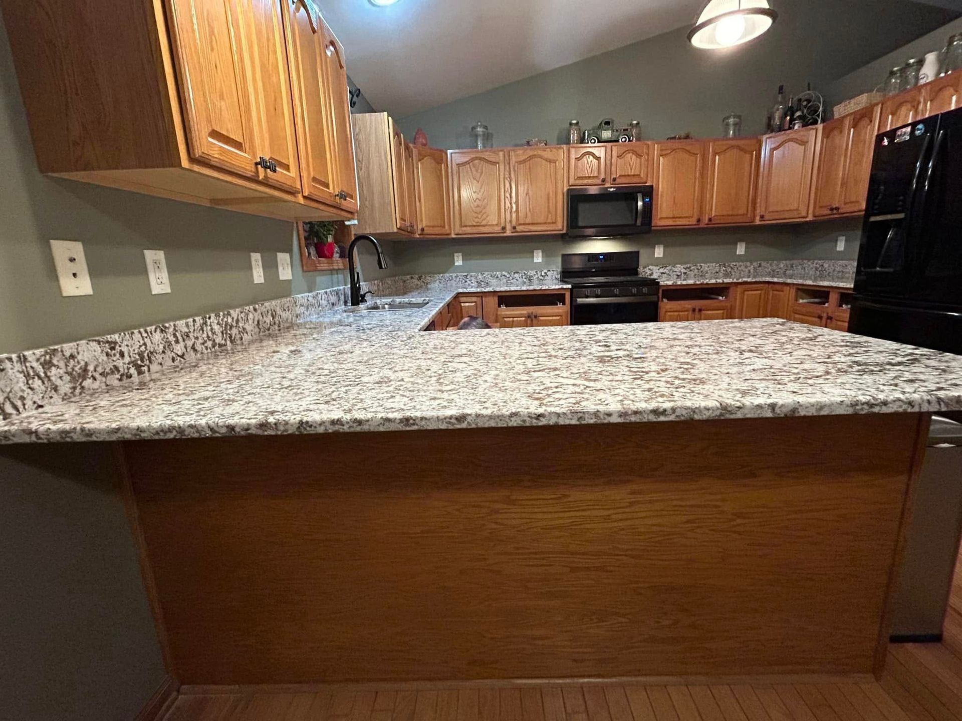 Modern kitchen with wood cabinets, granite countertops, black appliances, and an island in the foreground