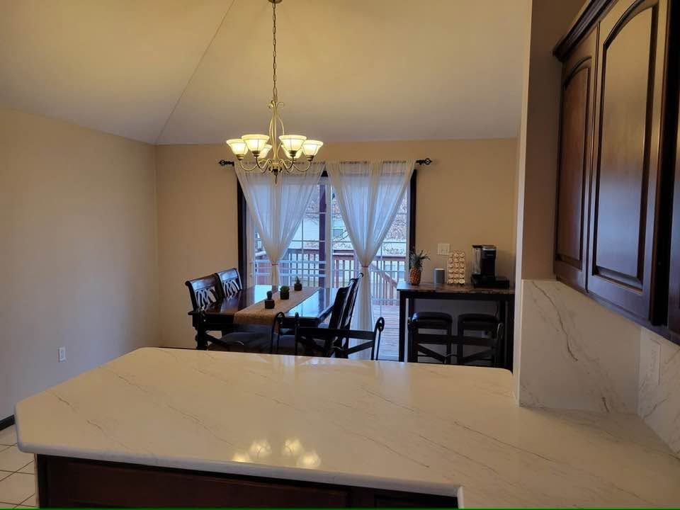 Dining room with a table, chandelier, and glass doors with curtains, viewed from a kitchen counter.
