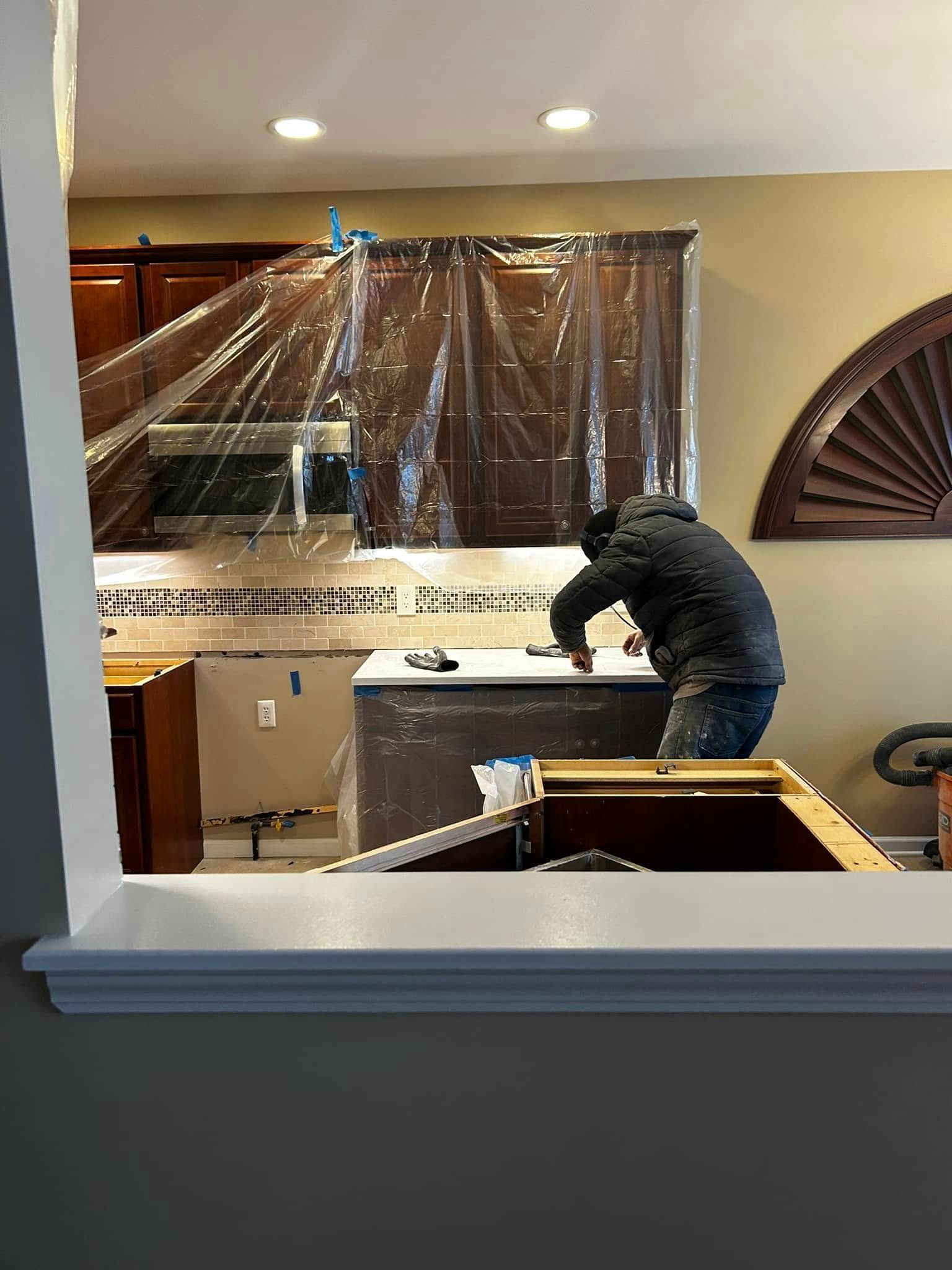 Worker inside a room, covered with plastic sheeting, leaning over a table during renovation.