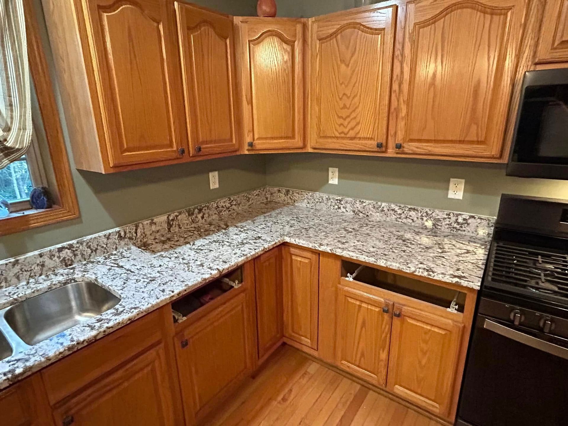 Kitchen corner with light wood cabinets, speckled granite countertops, stainless sink, and black appliances