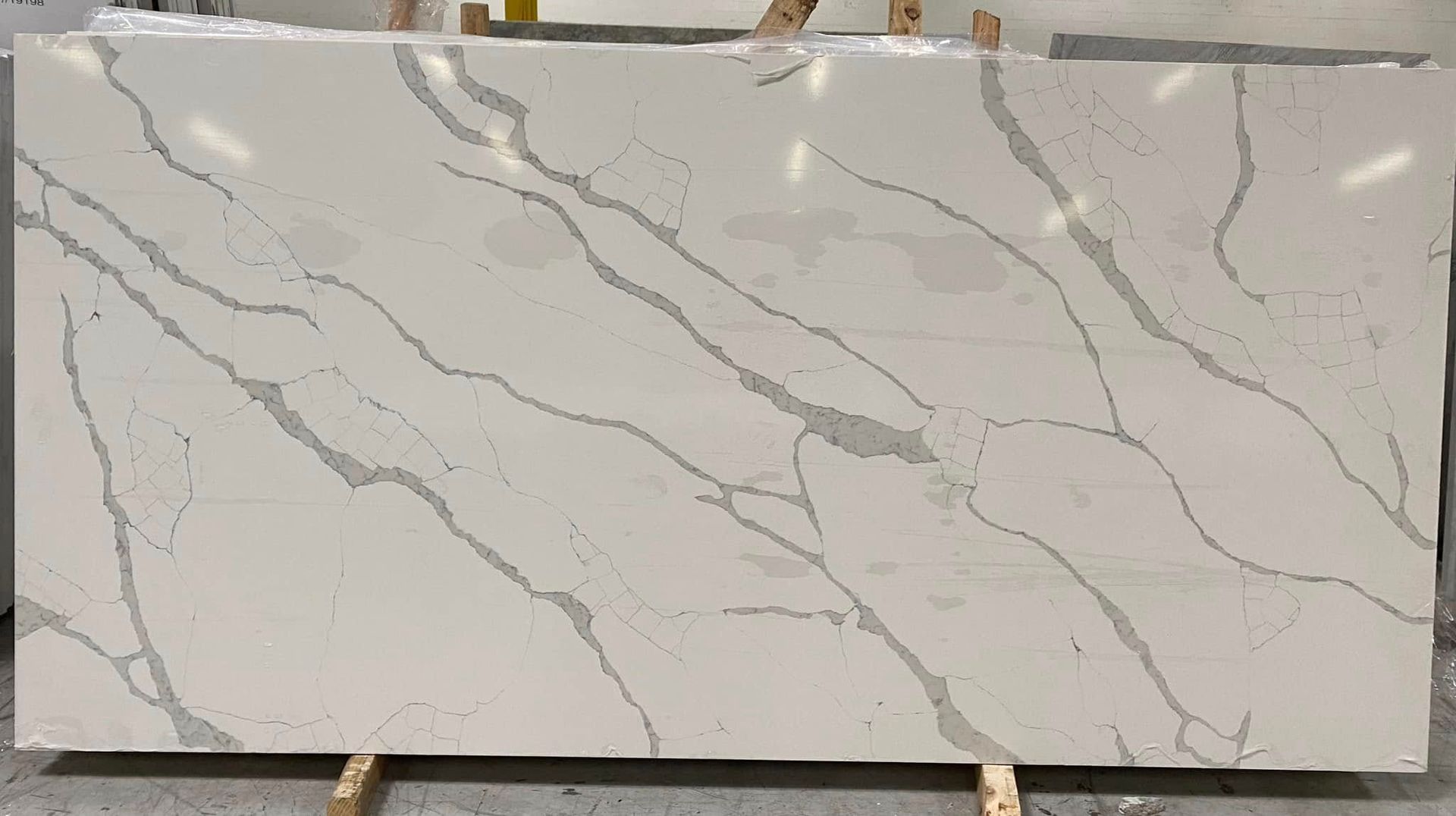 Rectangular white marble-look slab with thin gray veining, displayed on stands in a showroom.