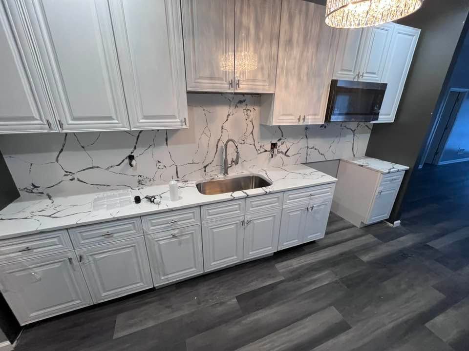 Modern kitchen with white cabinets, marble backsplash, stainless sink, and dark wood flooring