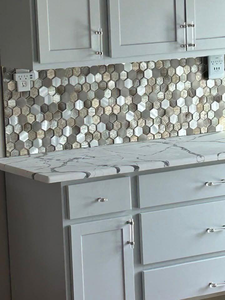 Gray kitchen cabinets with marble-look countertop and hexagon mosaic tile backsplash