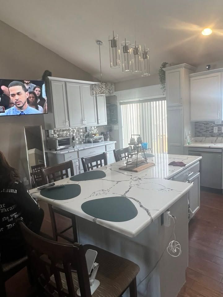 Bright kitchen with island, white cabinets, bar stools, and a wall-mounted TV showing a man.