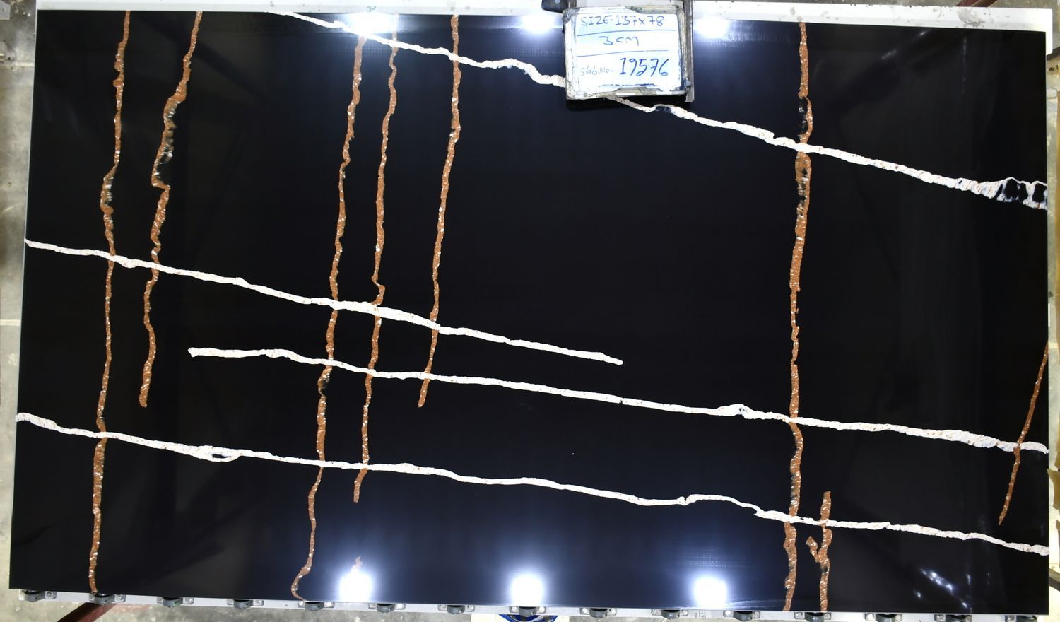 Dark reflective wall with tangled white and orange string lights and a small sign at the top center