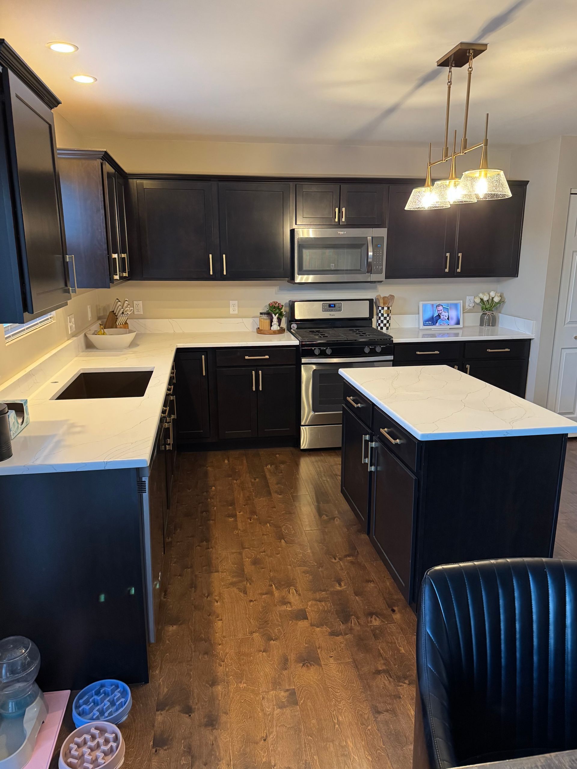 Modern kitchen with dark cabinets, white countertops, stainless appliances, and a central island.