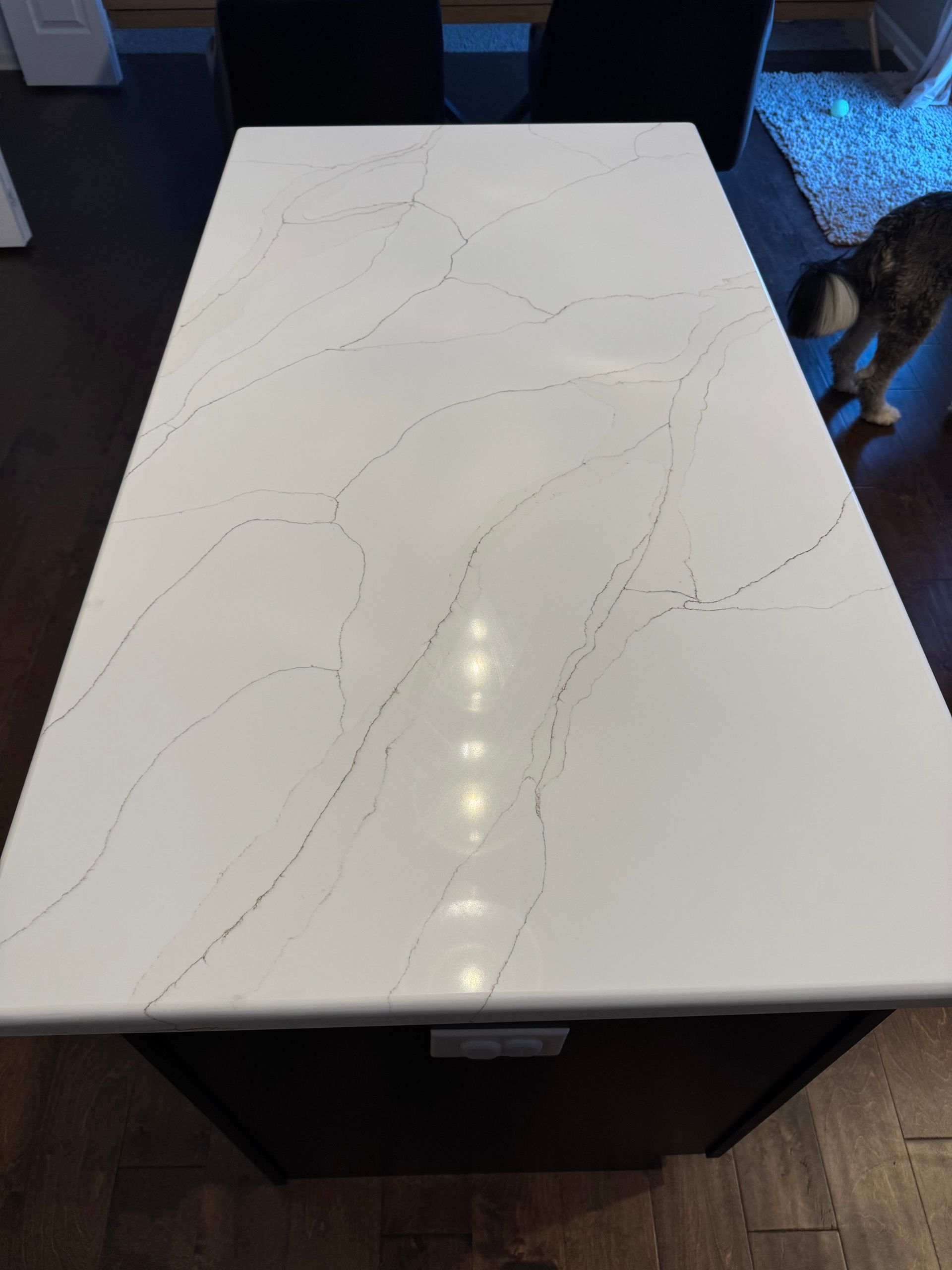 White glossy countertop with subtle gray veining, viewed from above in a room with a wooden floor.