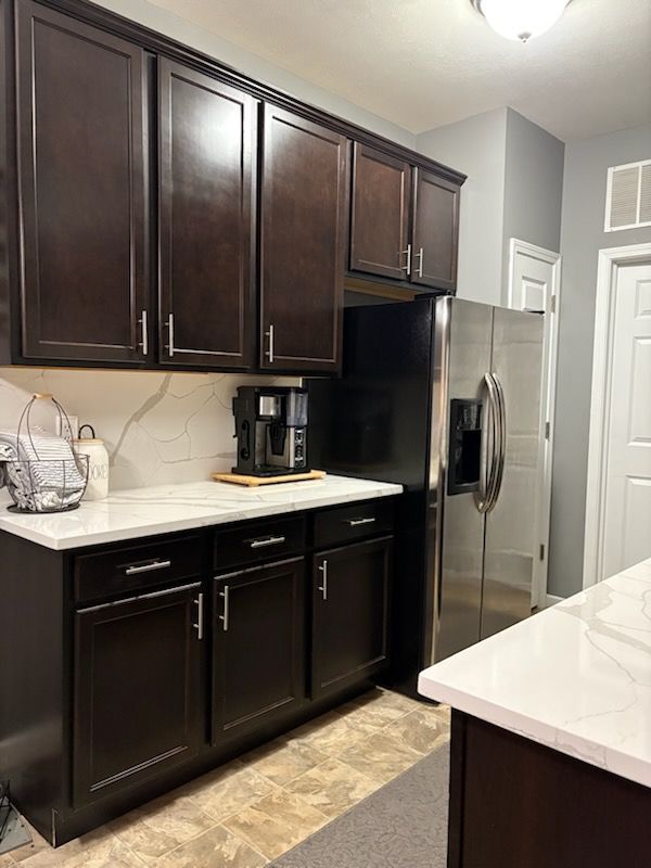 Dark wood kitchen cabinets with white countertops, stainless steel fridge, and coffee maker on the counter.