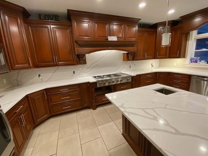 Modern kitchen with dark wood cabinets, white marble counters, and beige tile floor
