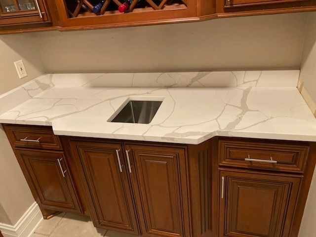 White marble-look countertop with a center sink and dark wood cabinets in a kitchen.
