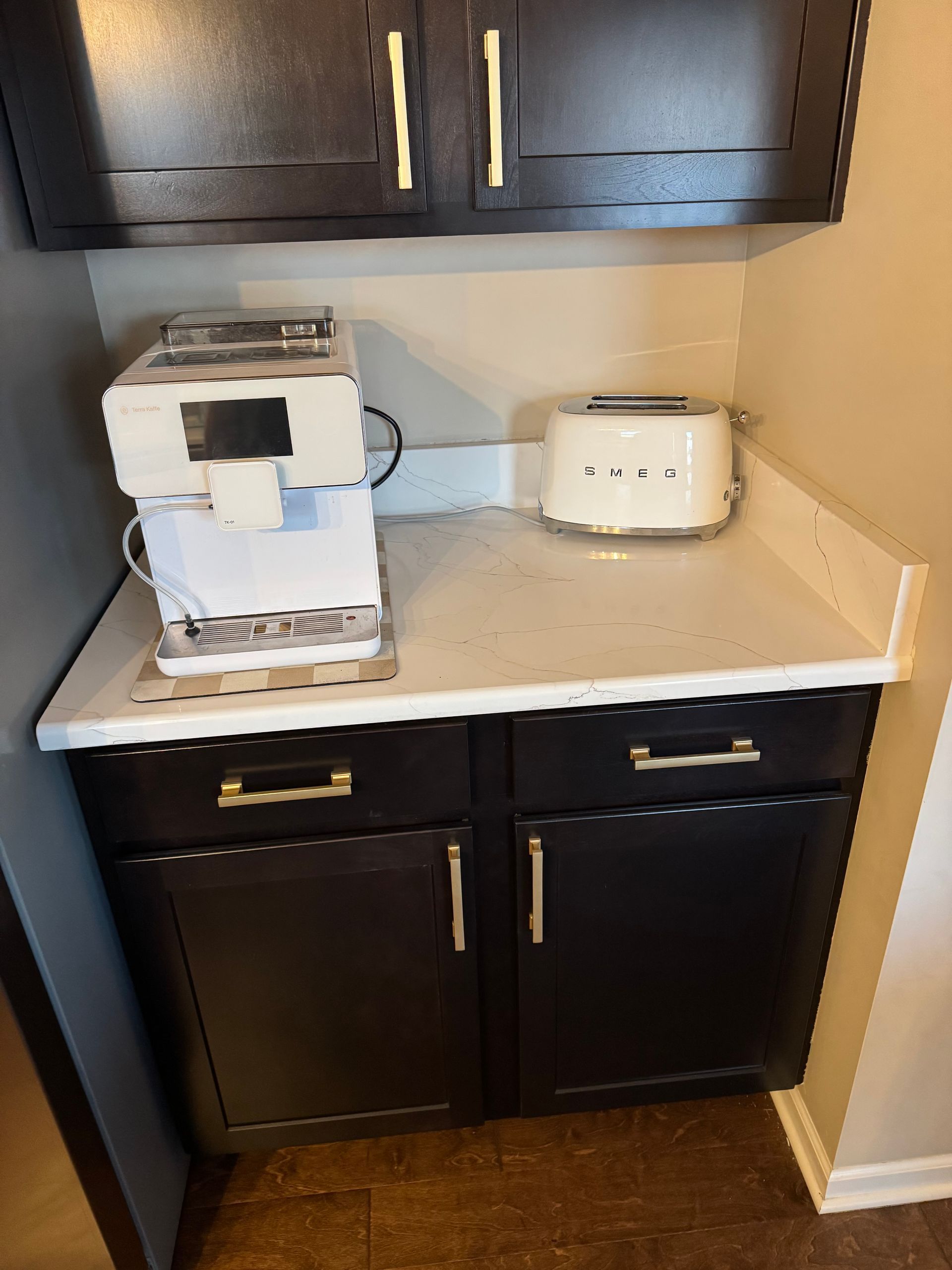 Kitchen counter with a white coffee maker and toaster under dark cabinets and black lower cabinets.