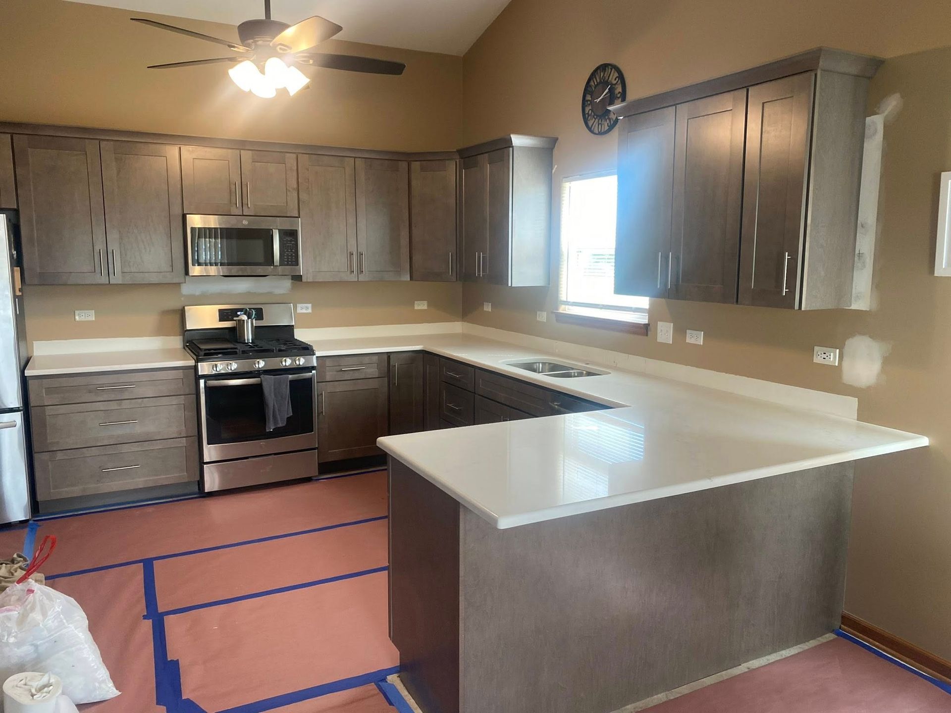Empty kitchen with gray cabinets, stainless steel appliances, and a white island under a ceiling fan.