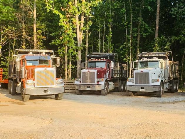 Three parked semi trucks on a dirt lot in a wooded area