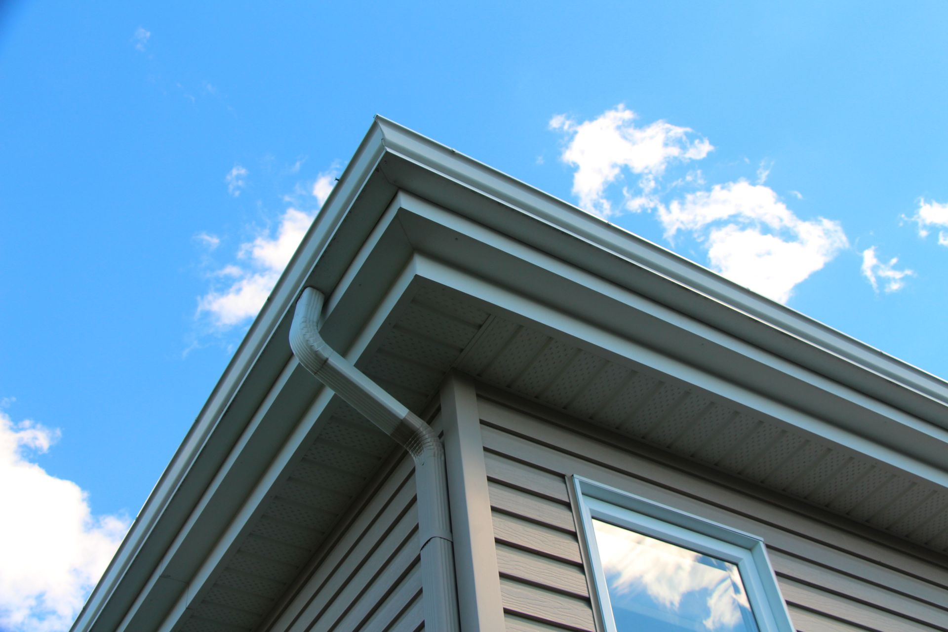 Corner of a house with gray siding and white trim under a blue sky with clouds
