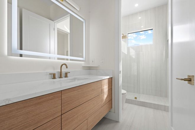 Modern white bathroom with wood vanity, mirror, brass faucet, and glass shower door.