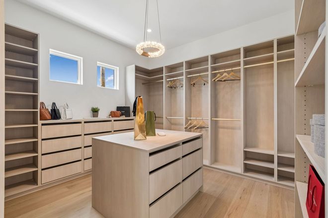 Spacious walk-in closet with white cabinetry, island, hanging rails, and light wood floors.