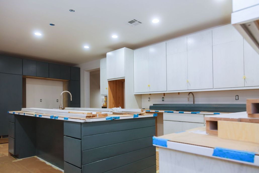 A kitchen under construction featuring dark blue cabinetry on the island and left wall, and white upper cabinets.