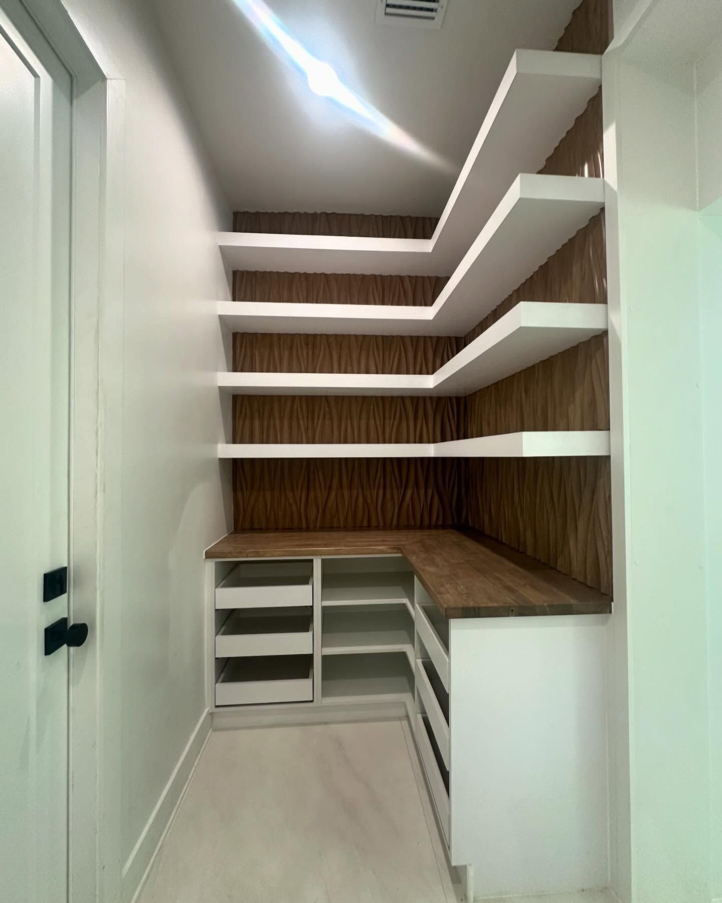 A walk-in pantry featuring white shelving units, drawers, and a wooden backsplash against a light-colored floor.