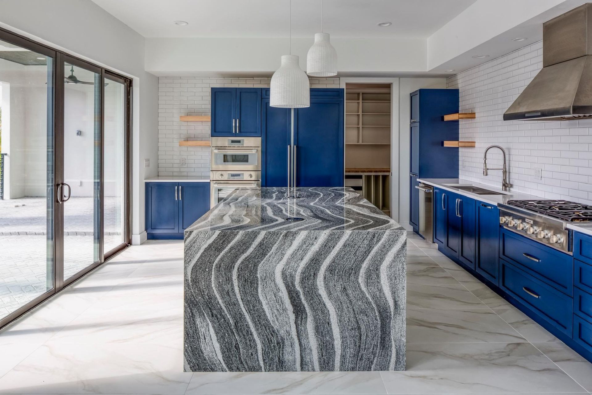 Modern kitchen with blue cabinets, a bold black-and-white wavy stone island, and a stainless steel range hood.