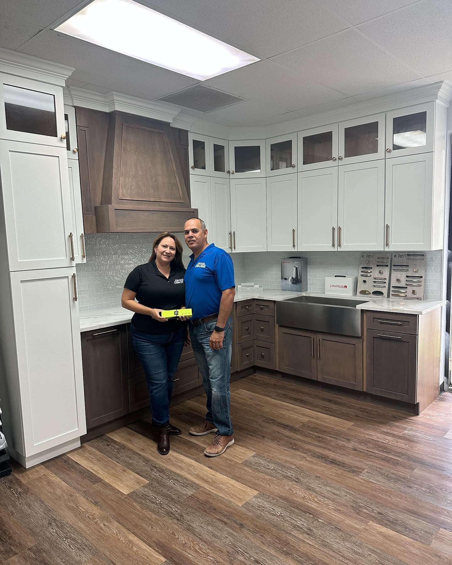 Two people in a showroom standing in front of custom white and wood-toned kitchen cabinetry.