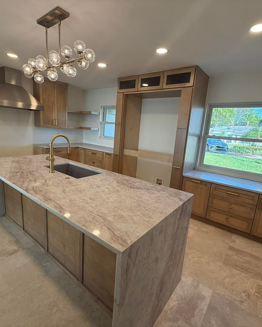 A modern kitchen with light wood cabinets, stone countertops, an island with a sink, and a multi-globe light fixture.