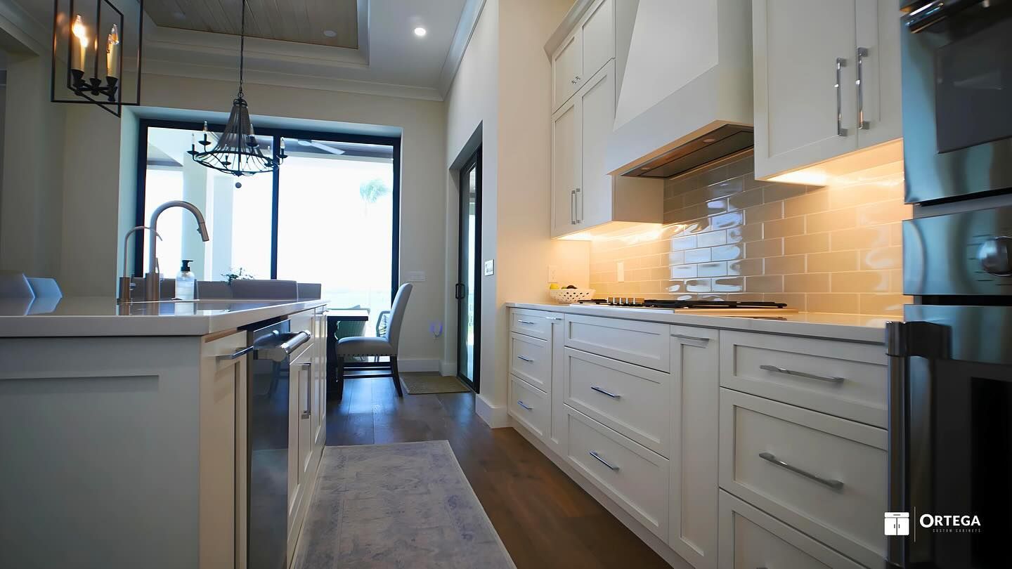 A modern kitchen featuring light-colored cabinetry, stainless steel appliances, and a dining area visible in the background.