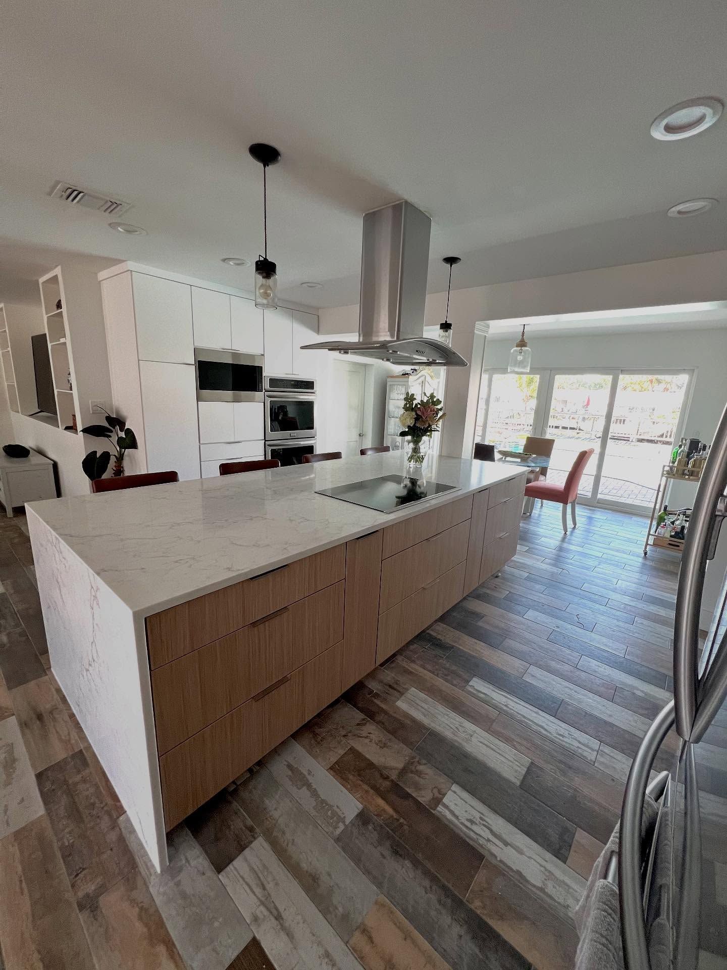 A modern kitchen with a large island featuring light wood cabinets and white countertops under hanging pendant lights.