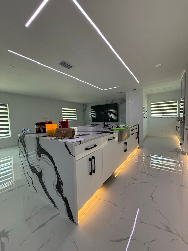 Modern kitchen featuring a large marble island with black veining, white cabinets, gold toe-kick lighting, and LED ceiling.