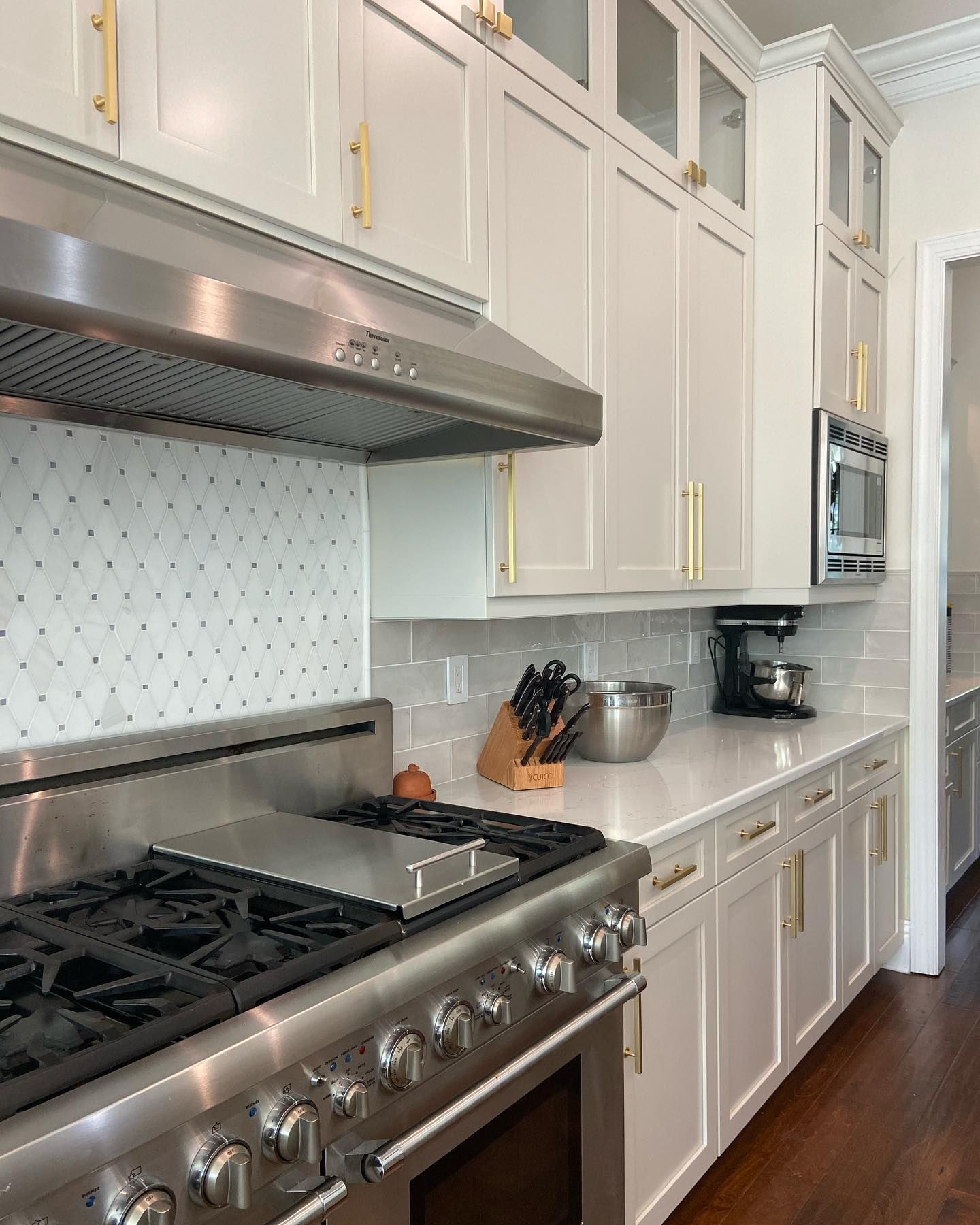 A stainless steel range stove and hood set against a white tile backsplash and custom kitchen cabinetry with brass pulls.