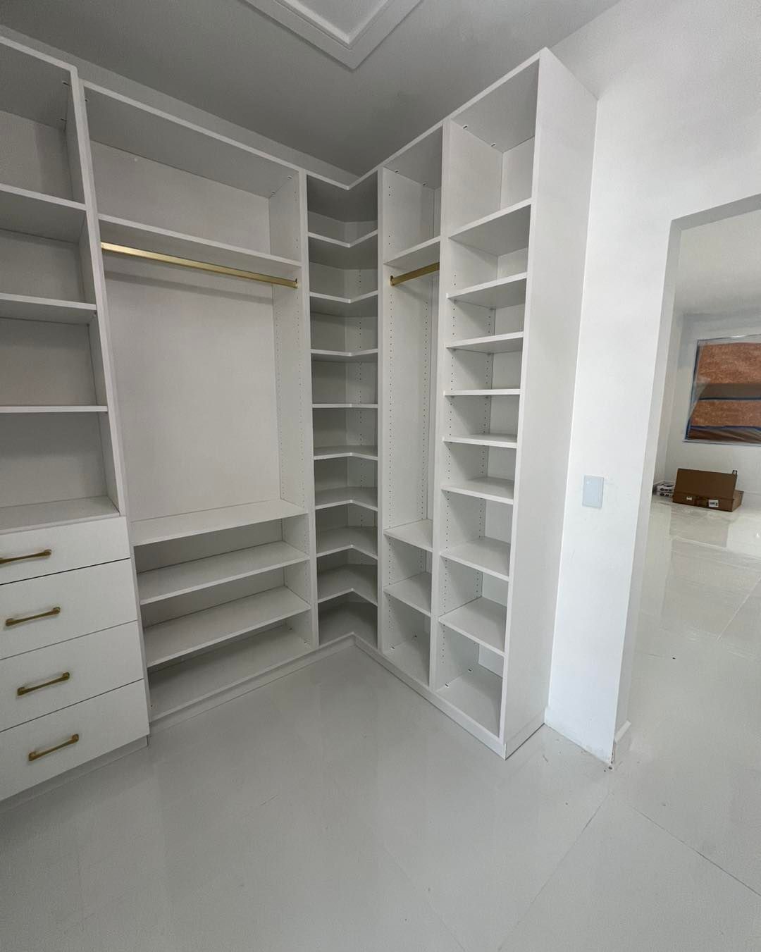 A bright white, L-shaped walk-in closet featuring open shelving, multiple drawers, and hanging rods.