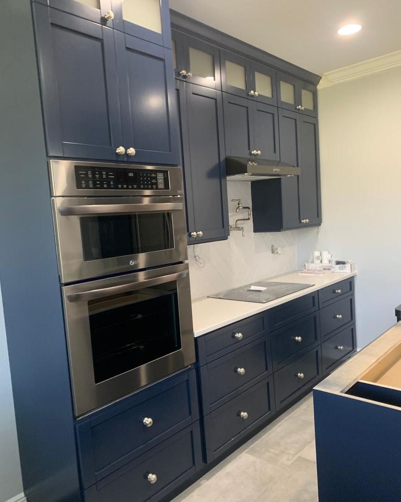 Navy blue kitchen cabinets with a built-in double oven, stainless steel appliances, and white countertops.