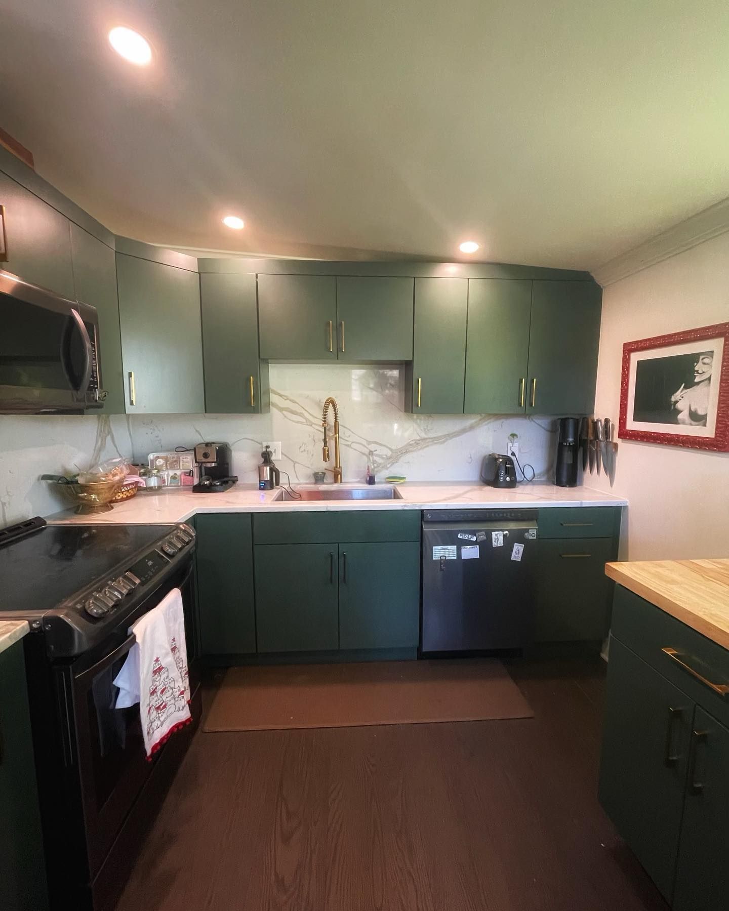 A kitchen featuring dark green cabinets, white countertops with a marble-patterned backsplash, and stainless appliances.