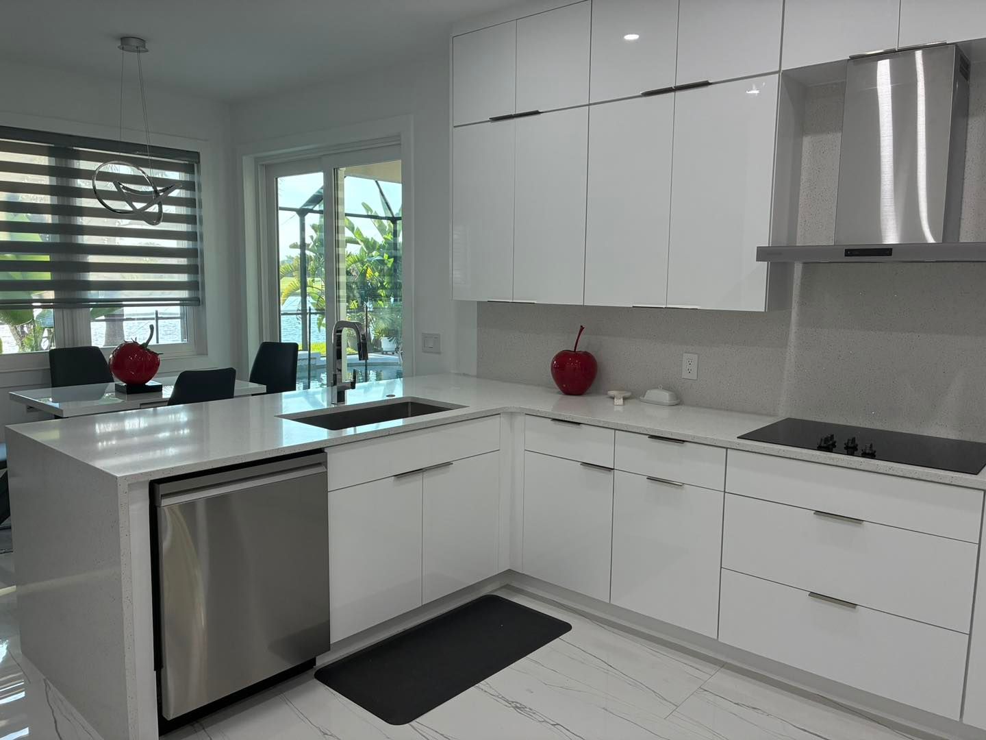 Modern white kitchen with glossy cabinets, stainless steel appliances, a kitchen island, and a dining area.