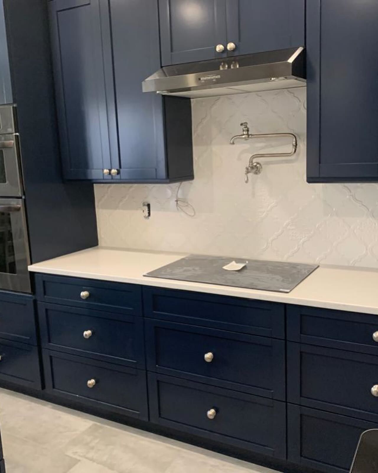 A modern kitchen featuring navy blue cabinets, a white countertop, a stainless steel range hood, and a wall-mounted faucet.