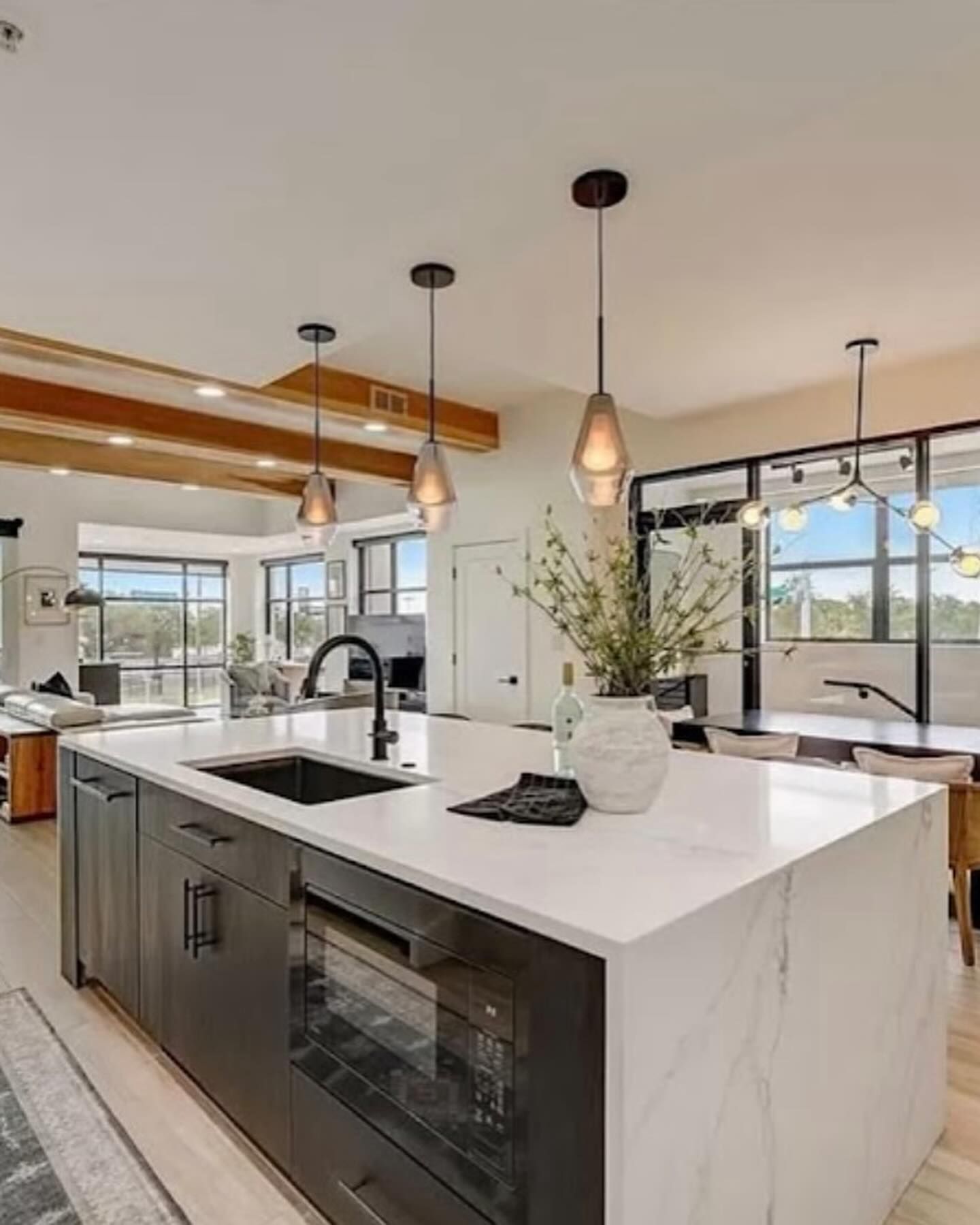 A modern kitchen island with dark cabinetry and a white marble countertop, featuring three pendant lights above.