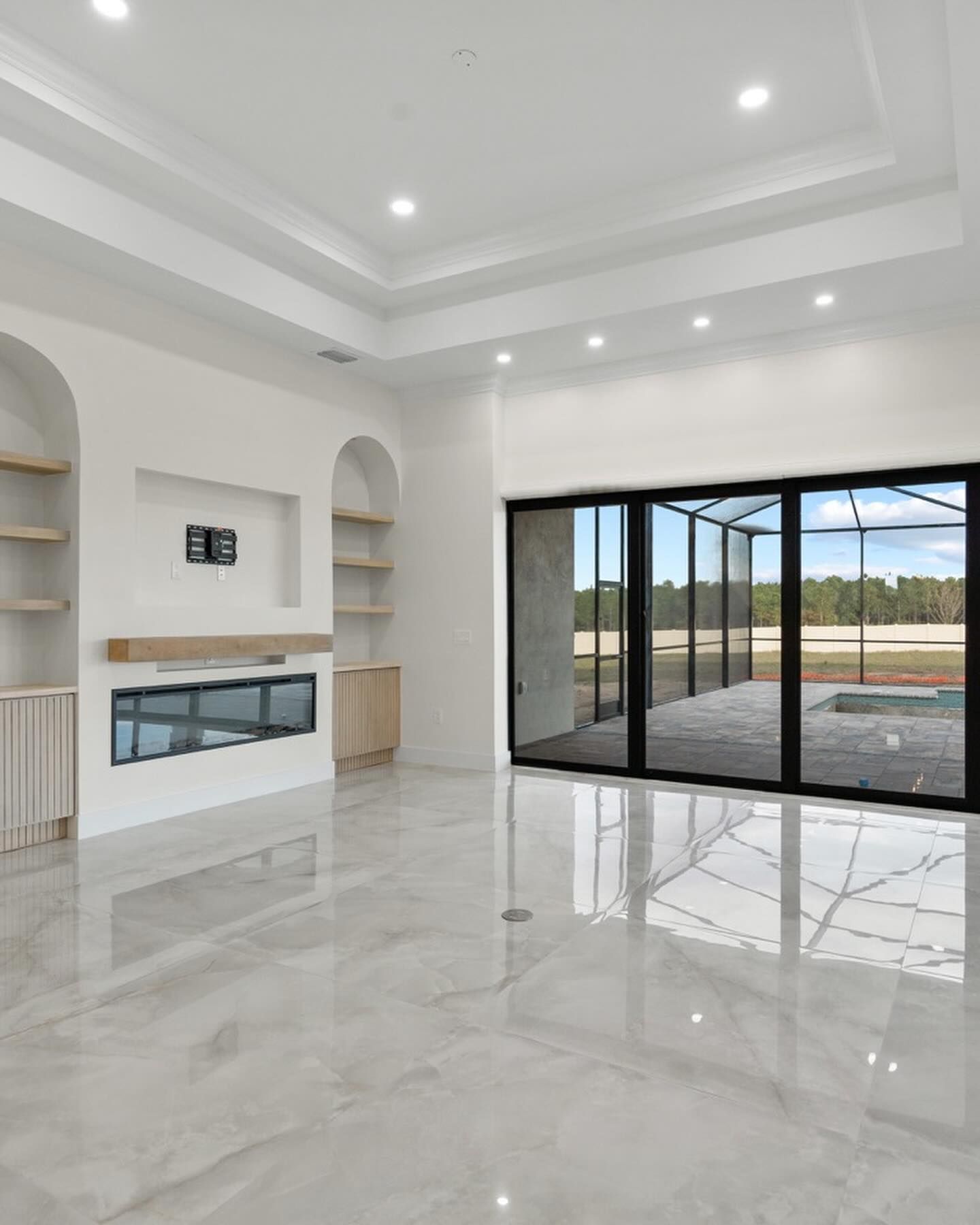 A modern living room with glossy white marble floors, a fireplace, arched shelving, and large glass sliding doors.