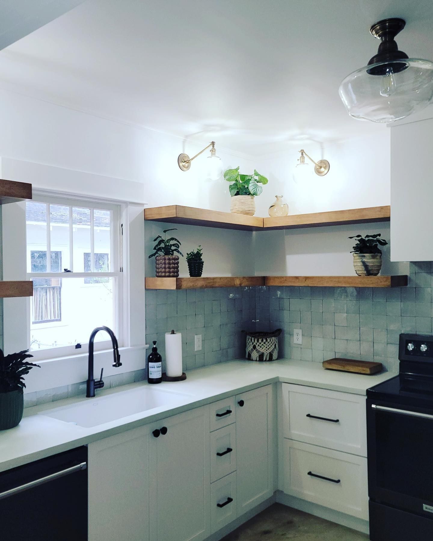 A bright kitchen featuring a white farmhouse sink, light blue square backsplash tiles, and natural wood corner shelving.