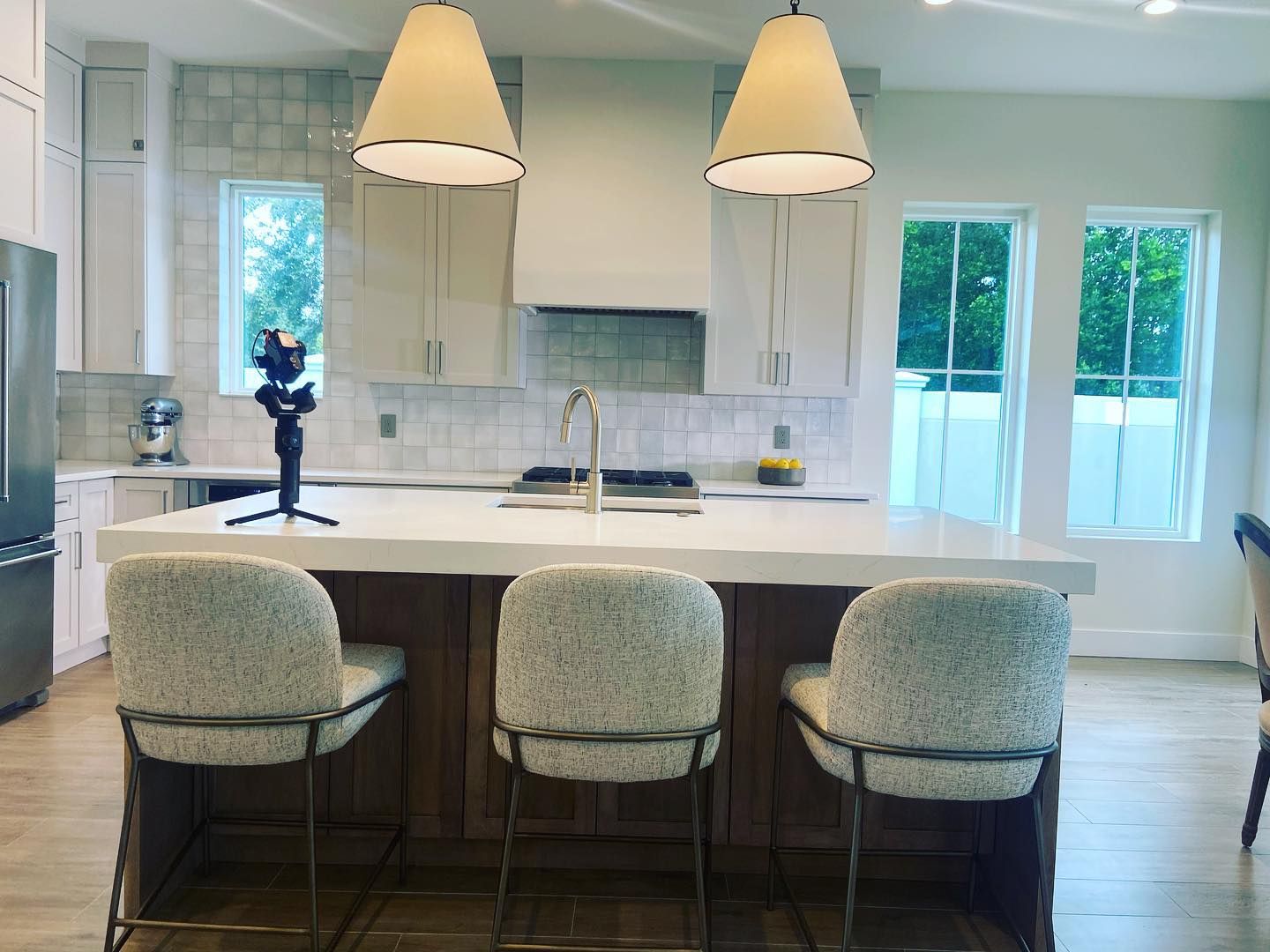 A kitchen island with three textured stools, a white countertop, and two pendant lights in a modern, bright kitchen.
