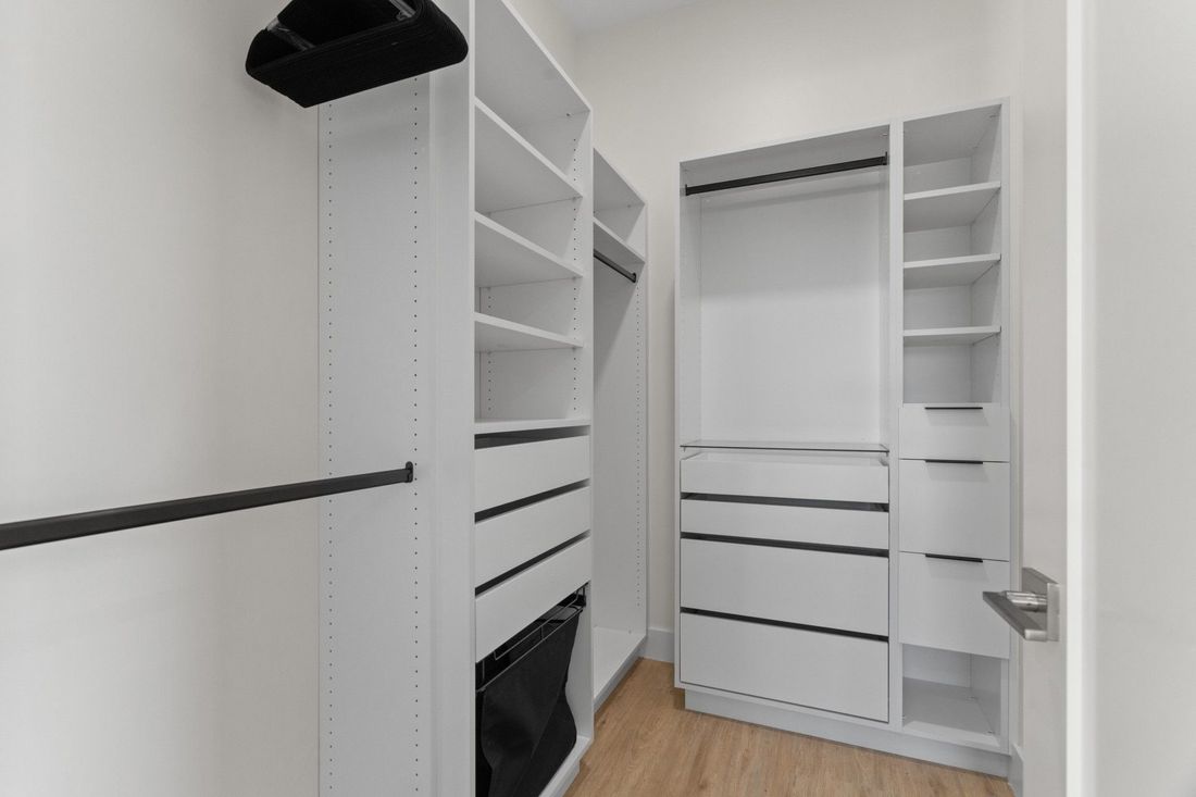White walk-in closet with shelves, drawers, hanging rods, and a wood floor.