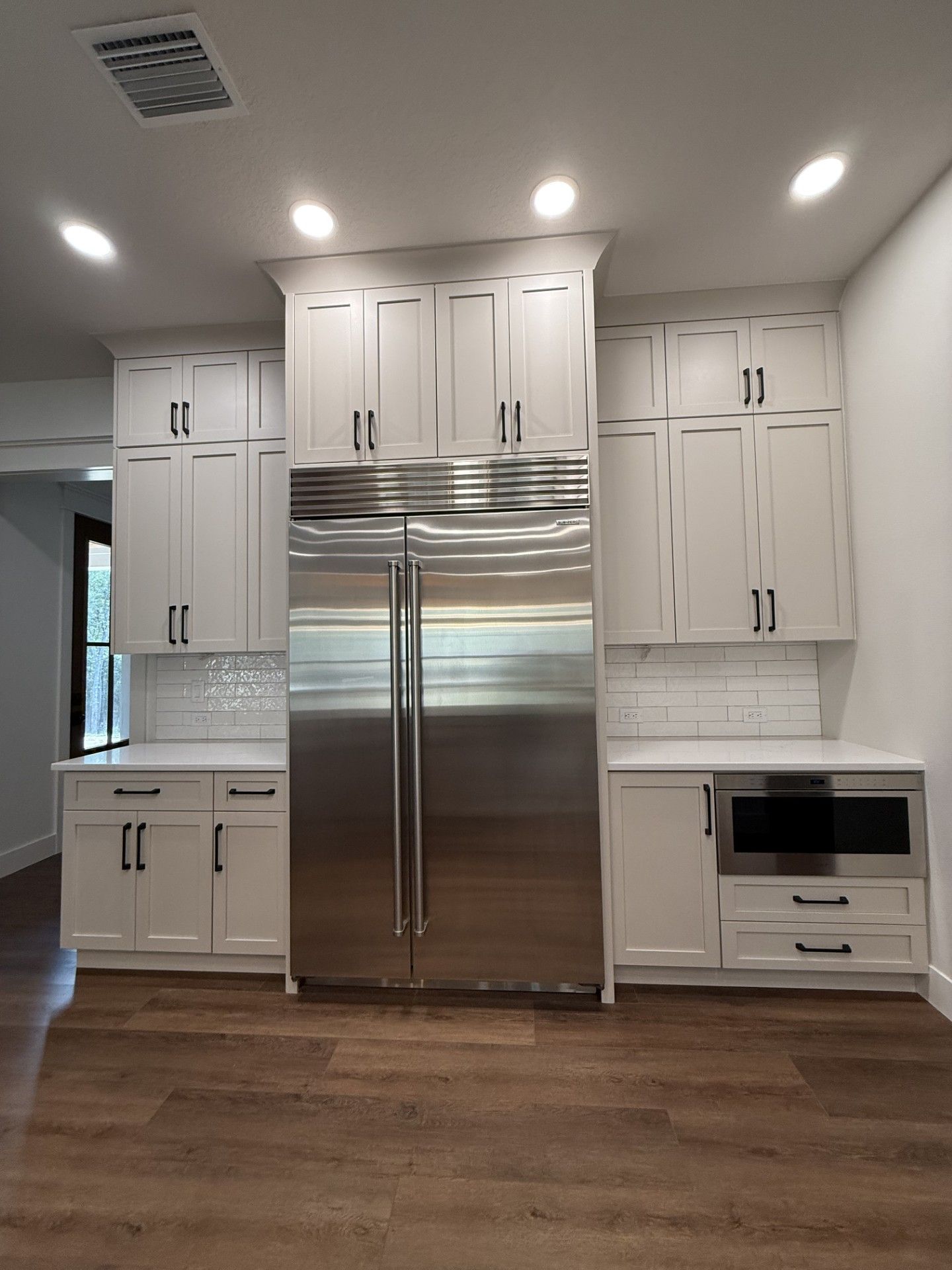 Modern kitchen with white cabinets, stainless steel refrigerator, built-in oven, and wood floors.